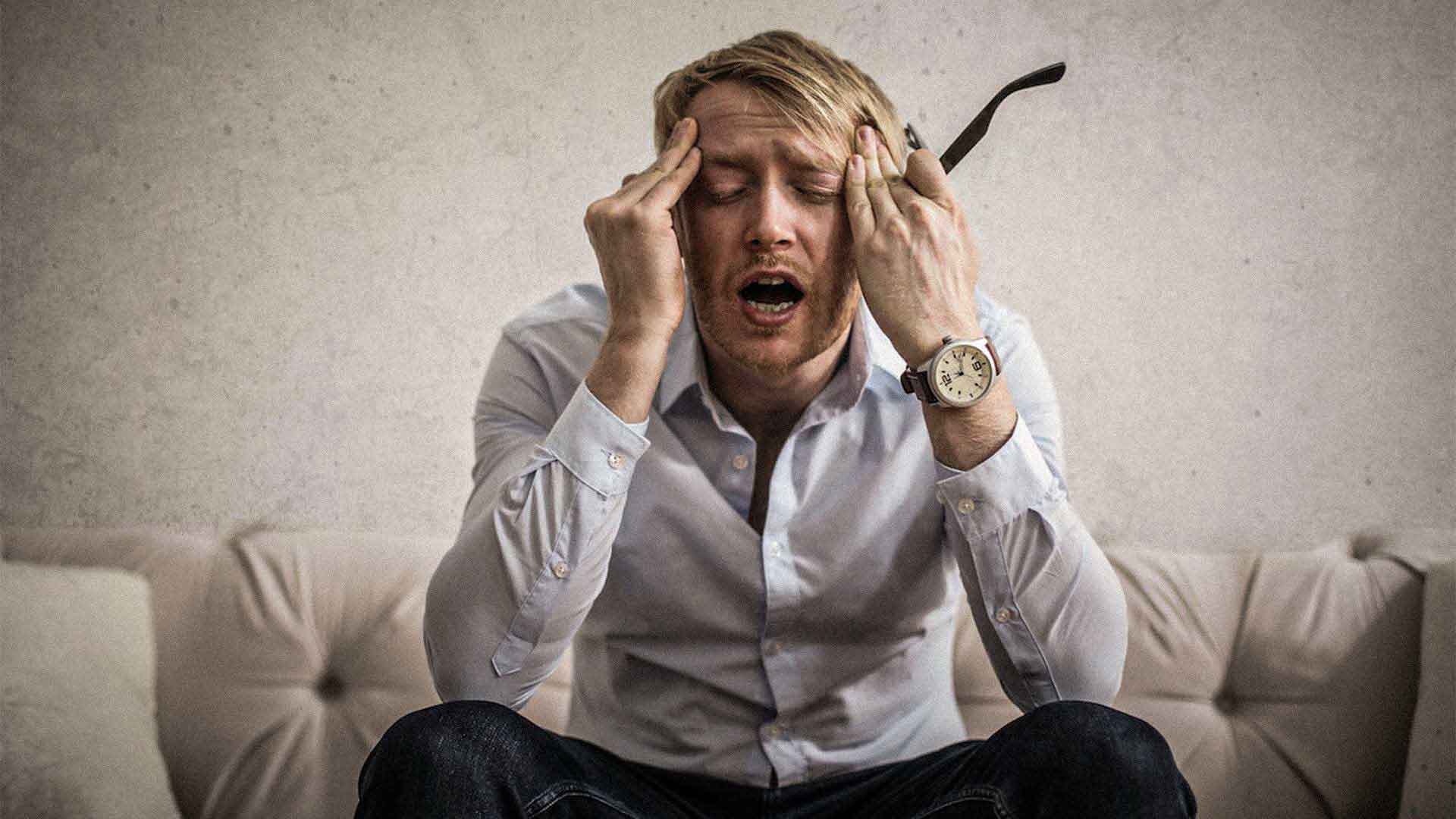 man appearing stressed holding his eye glasses