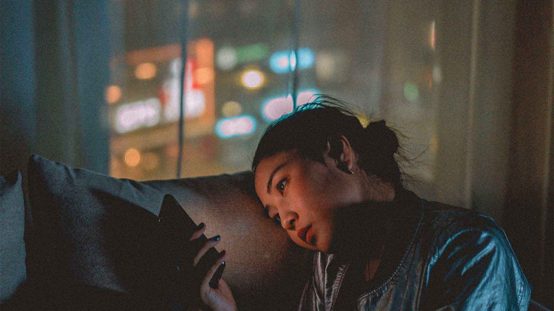 woman scrolling through her phone appearing tired